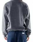 Back view of a woman wearing a gray sweatshirt and navy day pants on a white background