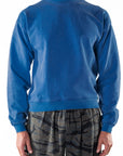 Person wearing a blue post surf crew sweatshirt and ocean tiger camouflage day pants on a white background