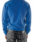 Back view of a person wearing a blue post surf crew sweatshirt and ocean tiger camouflage day pants on a white background