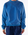 Person wearing a blue post surf crew sweatshirt and navy day shorts on a white background