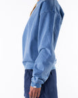 Side view of a woman wearing a blue sweatshirt and navy day shorts on a white background