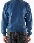 Person wearing a teal post surf crew sweatshirt and ocean tiger camouflage day shorts on a white background