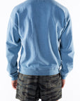 Back view of a person wearing a teal sweatshirt and ocean tiger camo day shorts on a white background