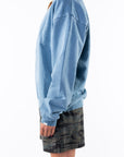 Side view of a woman wearing a teal sweatshirt and ocean tiger camo day shorts on a white background