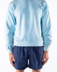 Person wearing a turquoise sweatshirt and navy day shorts on a white background