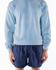 Person wearing a light blue ocean sweatshirt and navy day shorts on a white background