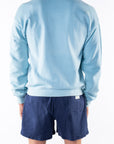 Back view of a person wearing a turquoise sweatshirt and navy day shorts on a white background