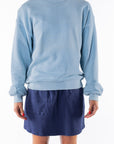Woman wearing a light blue ocean sweatshirt and navy day skirt on a white background