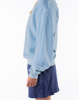 Side view of a woman wearing a light blue ocean sweatshirt and navy day skirt on a white background