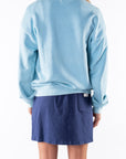 Back view of a woman wearing a turquoise sweatshirt and navy day skirt on a white background