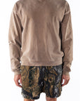 Person wearing a brown sweatshirt and real tree camouflage day shorts on a white background