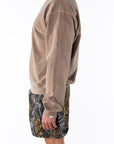 Side view of a person wearing a brown sweatshirt and real tree camouflage day shorts on a white background