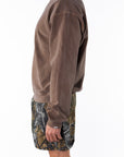 Side view of a person wearing a brown sweatshirt and real tree camouflage day shorts on a white background