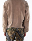 Back view of a person wearing a brown sweatshirt and real tree camouflage day shorts on a white background