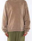 Woman wearing a brown post surf crw sweatshirt and army green day pants on a white background