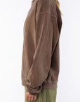 Side view of a woman wearing a brown oversized sweatshirt on a white background with army green day pants