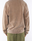 Back view of a woman wearing a brown post surf crew sweatshirt and army green day pants on a white background