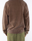 Back view of a woman wearing a brown sweatshirt and army green day pants on a white background