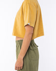 Side view of a woman wearing beach crop t-shirt in sunrise yellow with army green day pants
