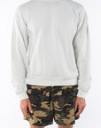 person wearing a beige sweatshirt and camouflage shorts on a white background