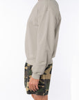 Side view of a person wearing a beige sweatshirt and camouflage shorts on a white background