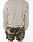 Back view of a person wearing a beige sweatshirt and camouflage day shorts on a white background
