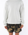 Woman wearing a beige sweatshirt and camouflage day shorts on a white background