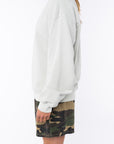 side view of a woman wearing a beige sweatshirt and camouflage day shorts on a white background