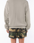 Back view of a woman wearing a beige sweatshirt and camouflage day shorts on a white background