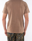 Back view of a person wearing a brown beach t-shirt and real tree camouflage day pants on a white background