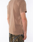 Side view of a person wearing a brown beach t-shirt and real tree camouflage day pants on a white background