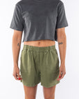 Woman wearing a gray beach crop t-shirt and army green day shorts on a white background
