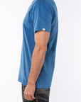 Side view of a man wearing a teal beach t-shirt with ocean tiger camo day pants on a white background