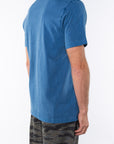 Side back view of a man wearing a teal beach t-shirt with ocean tiger camo day pants on a white background