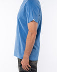 Side view of a man wearing a blue beach t-shirt with ocean tiger camo day pants on a white background