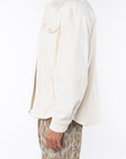 Side view of a man wearing a beige bucky shirt jacket, brown beach t-shirt and leopard camo printed day shorts on a white background