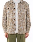 Person wearing a leopard camo bucky patterned jacket over a white shirt with army green day pants on a white background