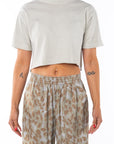 Person wearing a light gray cropped t-shirt and leopard camo patterned pants on a white background