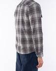 Side back shot of a man wearing lightweight flannel plaid shirt in Black/red with navy pants on a white background.