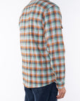 Side back shot of a man wearing a lightweight flannel plaid shirt in Orange/Green with navy pants on a white background.