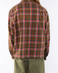 Back shot of a woman wearing the Bucky Flannel Over shirt in brown/red with army green day pants.