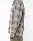 Side shot of a woman wearing the a lightweight flannel Plaid Shirt in green/red with army green pants on a white background.