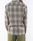 Back shot of a woman wearing a lightweight flannel plaid shirt in green/red with army green pants on a white background