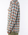 Side shot of a woman wearing a lightweight flannel plaid shirt in green/orange with army green pants on a white background.