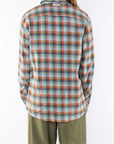 Back shot of a woman wearing a lightweight flannel plaid shirt in green/orange with army green pants on a white background