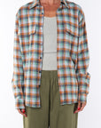 Woman wearing a lightweight flannel plaid shirt in green/orange over a v-neck Tank in cream with army green pants on a white background