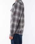 Side shot of a woman wearing a lightweight flannel plaid shirt in black/red with navy pants on a white background