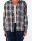 Woman wearing a lightweight flannel plaid shirt in black/red over a v-neck Tank in cream with navy pants on a white background