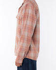 Side shot of a woman wearing a lightweight flannel plaid shirt in orange/blue with navy pants on a white background
