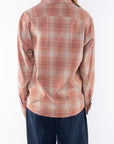 Back shot of a woman wearing a lightweight flannel plaid shirt in orange/blue with navy pants on a white background